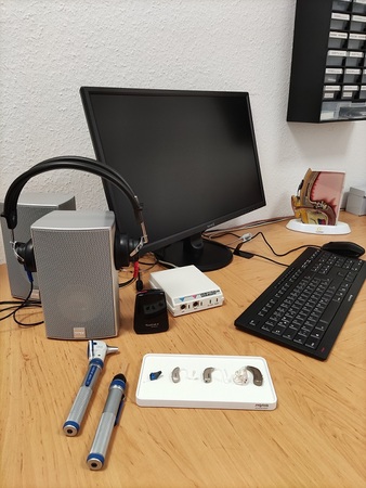 Modern ausgestatteter Arbeitsplatz eines Hörakustikers mit Bildschirm, Hörgeräten und Zubehör.